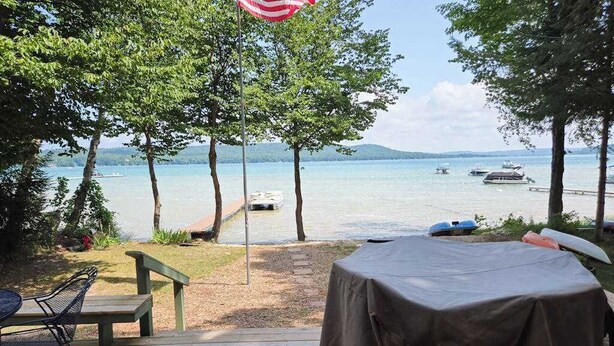 A deck with a table and chairs overlooking a lake with boats. - Glen Lake Home w/private beach frontage and dock (Empire)