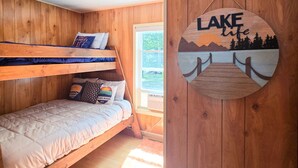 A cabin with wooden walls, a bunk bed, a window with a view, and a wall decoration reading 'LAKE life'. - Glen Lake Home w/private beach frontage and dock (Empire)