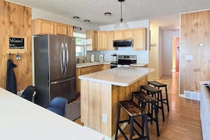 Una cocina moderna con armarios de madera, un refrigerador de acero inoxidable, un microondas y una isla central con taburetes.