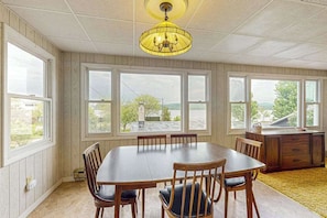 Une salle à manger avec une grande table, des chaises, un lustre et une vue dégagée grâce à de grandes fenêtres.