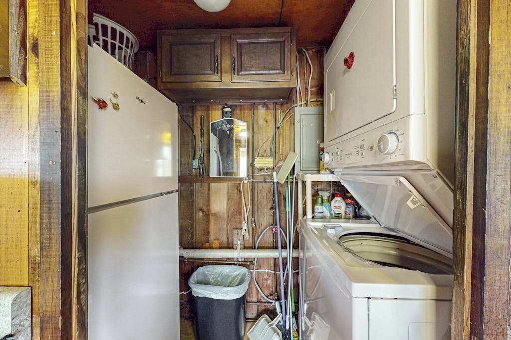 A compact kitchen with a refrigerator, washing machine, and wooden cabinets.