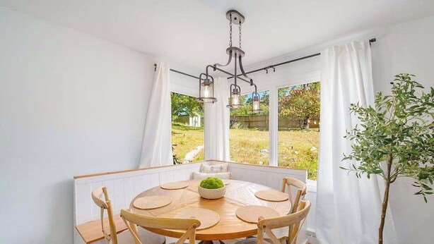 Zona pranzo con tavolo rotondo in legno, sei sedie in legno, un lampadario e una pianta in vaso.
