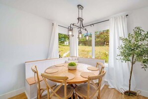 Uma sala de jantar com uma mesa redonda de madeira, seis cadeiras de madeira, um candelabro e um vaso com planta.