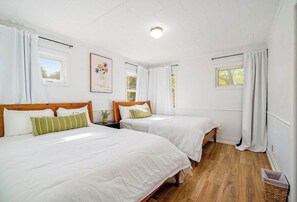 A room with two beds, white bedding, wooden headboards, a framed picture, and a window with curtains. - Comfortable home in a great location with enclosed yard, family room, & kayaks (Frankfort)