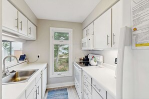 Una cocina moderna con armarios blancos, un lavamanos de acero inoxidable, un microondas y una ventana con vistas a árboles.