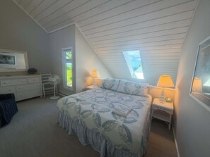 A bedroom with a bed, two bedside lamps, a dresser, a desk, and a window with a view. - Beautiful beachfront townhouse with deck, water views, community firepit (Glen Arbor)