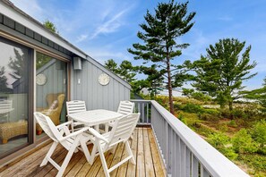A wooden deck with a table and chairs, overlooking a natural landscape with trees and a body of water. - Beautiful beachfront townhouse with deck, water views, community firepit (Glen Arbor)