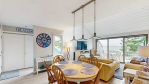 Un salon moderne avec une table de salle à manger ronde, des chaises en bois, un canapé et une grande fenêtre donnant sur un paysage agréable.