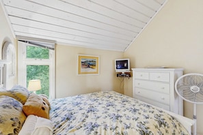 Un dormitorio con cama, cómoda, televisor y ventana con persianas.