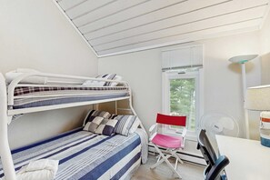 Ein Schlafraum mit Etagenbetten, einem Schreibtisch, einem Stuhl und einem Fenster mit Jalousien.