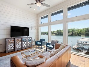 A spacious living room with a large TV, comfortable seating, and a view of a lake.