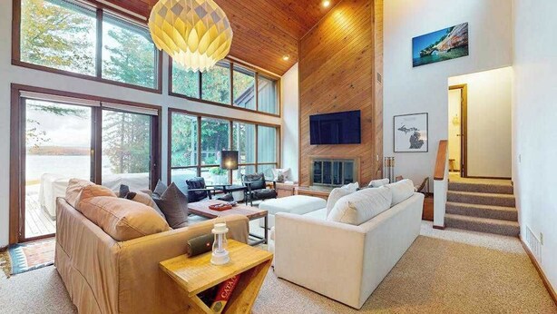 Un salón amplio con ventanas grandes, chimenea y techo de madera.