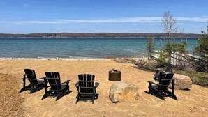 Una playa con cuatro sillas Adirondack negras, un brasero y una gran roca.