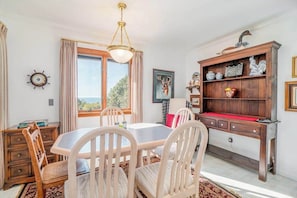 Un comedor con una mesa y sillas, un aparador de madera con objetos decorativos, y vista al exterior por la ventana.