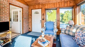 A wooden interior with a television, a plaid armchair, a sofa, and a door leading outside.