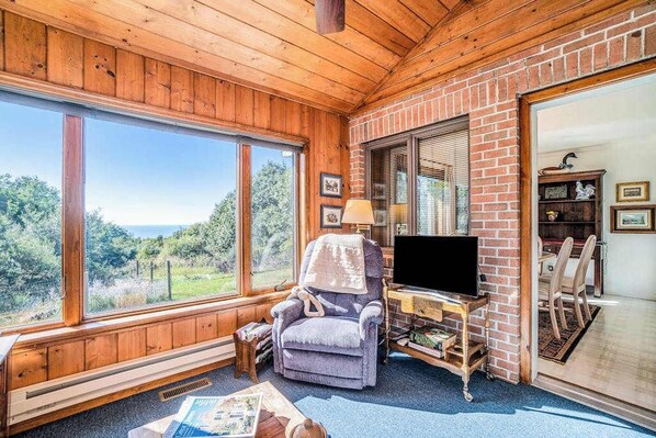 Una habitación acogedora con un ventanal grande, un televisor sobre un mueble de madera, una silla y una estantería.