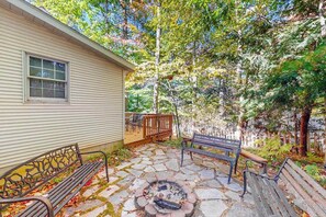 A stone patio with a fire pit, two benches, and a wooden deck. - Lovely home in downtown Glen Arbor with deck, gas grill, washer/dryer, and AC (Glen Arbor)