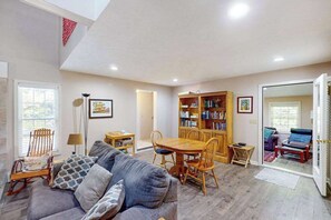 A spacious living area with a sofa, dining table, chairs, a bookshelf, and a view through an open door. - Lovely home in downtown Glen Arbor with deck, gas grill, washer/dryer, and AC (Glen Arbor)