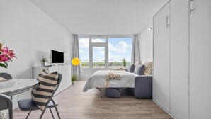 A modern bedroom with a bed, bedside table, TV, and a view of the outdoors. - Cozy Holiday Apartment with Limited Sea View near the Beach in Wendtorf (Wendtorf)