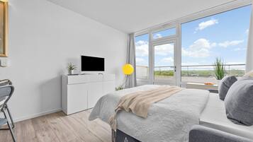 Ein modernes Schlafzimmer mit Bett, Fernseher, Schreibtisch und Fenster mit Blick.