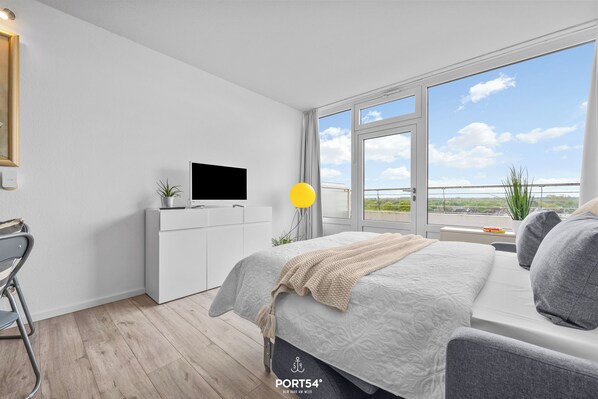 A modern bedroom with a bed, a TV, a desk, and a window with a view. - Cozy Holiday Apartment with Limited Sea View near the Beach in Wendtorf (Wendtorf)