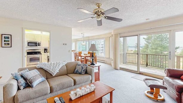 A living room with a sofa, a coffee table, a ceiling fan, and a view of a balcony. - Lovely Lake Michigan beachfront condo with deck, washer/dryer, fireplace, views (Glen Arbor)
