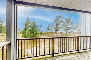 A covered outdoor area with a wooden deck and a view of trees and open land. - Lovely Lake Michigan beachfront condo with deck, washer/dryer, fireplace, views (Glen Arbor)