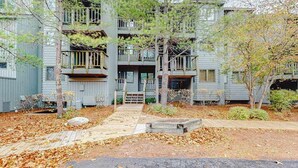A multi-story residential building with balconies, a wooden pathway, and a small garden area. - Lovely Lake Michigan beachfront condo with deck, washer/dryer, fireplace, views (Glen Arbor)