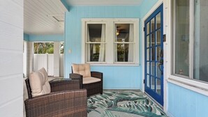 Een overdekt terras met rieten meubilair, een blauwe deur en een raam met gordijnen.