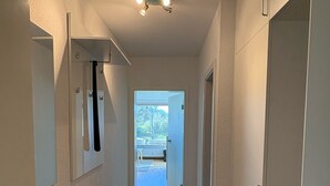Een smalle gang met een houten bankje, een kleed en een deur naar een buitenruimte.