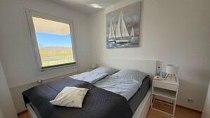 Een slaapkamer met een bed, een raam met uitzicht, een schilderij, een nachtkastje en een lamp.