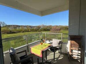 Un balcon avec une table et des chaises, une vue sur un champ verdoyant et, au loin, une rangée d’éoliennes.