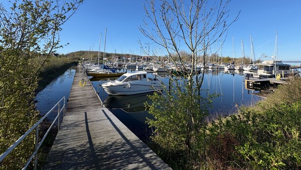 Een jachthaven met aangemeerde boten, een houten steiger en een heldere lucht.