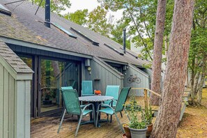 A house with a sloped roof, a covered patio with a table and chairs, and a large window. - River-view condo with fireplace, deck, washer/dryer, and community firepit (Glen Arbor)