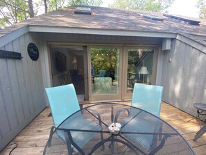 Eine überdachte Terrasse mit einem Metalltisch und -stühlen, einem Glastür-Eingang und einem Holzboden.