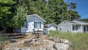 A small, rustic cabin with a stone-paved entrance, surrounded by large rocks and tall grass.