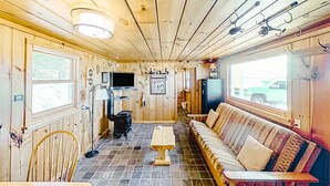 A cabin interior with a wooden ceiling, a sofa, a TV, and a window.