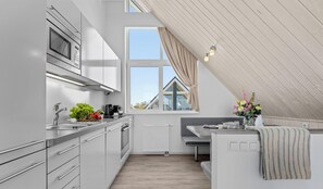 Una cocina moderna con horno empotrado, una ventana con cortinas y una zona de comedor con banco.