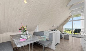 Un comedor moderno con techos altos, una mesa para dos y vistas al mar.