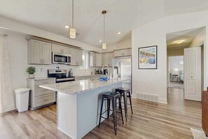 A modern kitchen with white cabinets, a large island with bar stools, a microwave, and a refrigerator. - Charming 2BR/2BA Condo 1 Mile from Lake Michigan, with shared pool (Douglas)