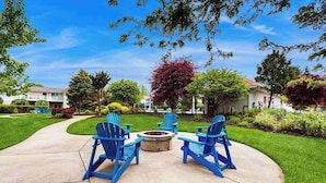 Un patio con sillas Adirondack azules y un pozo de fuego.