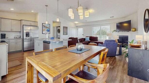 Una cocina moderna con electrodomésticos de acero inoxidable, un comedor con mesa de madera y una sala de estar con televisor y asientos.