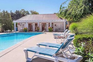 A pool area with lounge chairs and a building with a tiled roof. - Charming 2BR/2BA Condo 1 Mile from Lake Michigan, with shared pool (Douglas)