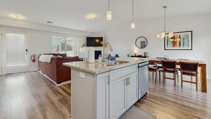 Una cocina moderna con una isla central, muebles blancos e iluminación colgante.