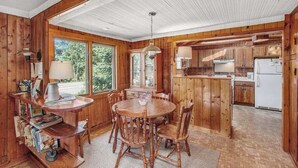 Ein Holzblock-Interieur mit Esstisch, Stühlen, Küchenzeile und großem Fenster.