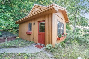 Una pequeña cabaña de madera con puerta roja, ventanas y un porche con macetas de flores.