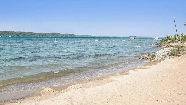 Ein Strand mit klarem Wasser, einem sandigen Ufer und Hügeln in der Ferne.