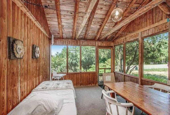 Una cabaña de madera con una cama, una mesa y ventanas amplias.