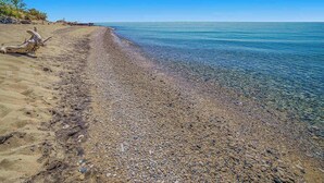 A pebbly beach with clear water, a driftwood piece, and a clear sky. - Cabin-style cottage w/ full kitchen, wood-burning fireplace, and full WiFi (Frankfort)