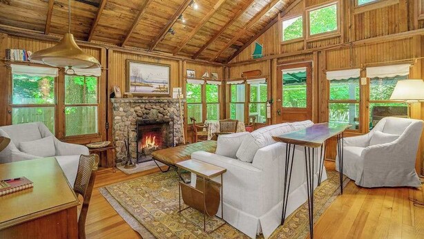 A rustic cabin interior with a stone fireplace, wooden walls, and large windows. - Cabin-style cottage w/ full kitchen, wood-burning fireplace, and full WiFi (Frankfort)